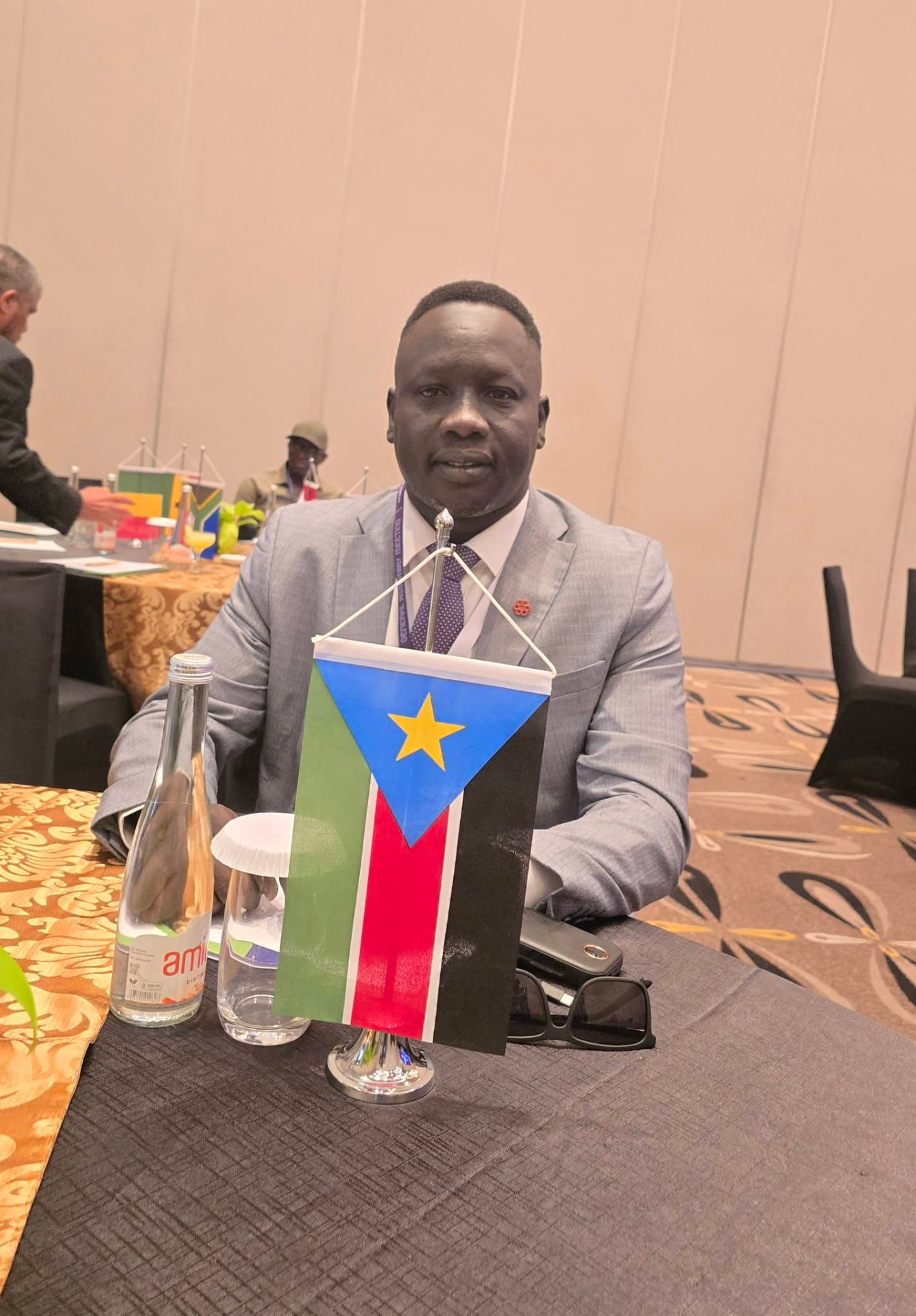 SSMF delegate seated with the South Sudan flag at an international sports meeting